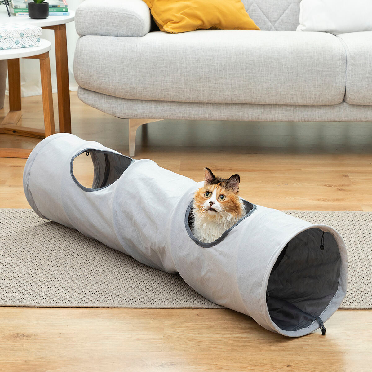 Túnel plegable para gatos Nuzzo en un salón con un gato asomado