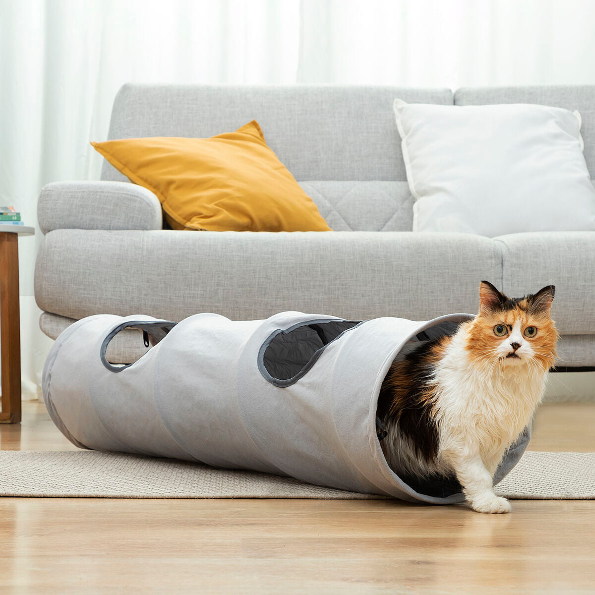 Túnel plegable para gatos Nuzzo en un salón con un gato asomado